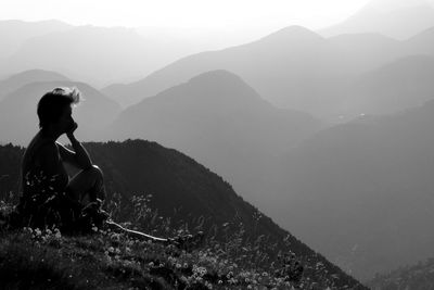 Silhouette of woman sitting on rock against mountains