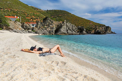 Woman lying down on beach against sky