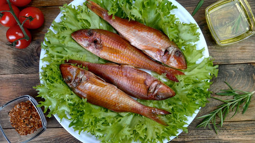 Smoked whole sea fish served salad leaves with vegetable and spices on white dish.