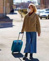Senior 60s woman with blue suitcase traveling alone during coronavirus epidemic