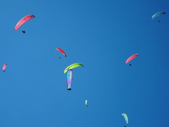 Low angle view of parachutes flying against clear blue sky