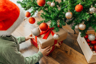 A boy, a child takes out a christmas present from under the new year tree, a box with a red ribbon.