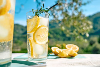 Summer refreshing lemonade drink or alcoholic cocktail with ice, rosemary and lemon slices on table