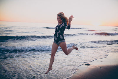 Full length portrait of young woman jumping on beach