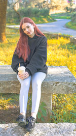 Portrait of young woman sitting on retaining wall