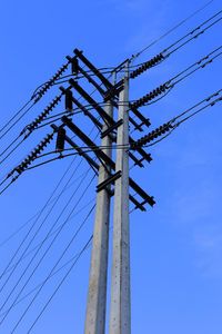 Low angle view of electricity pylon against blue sky