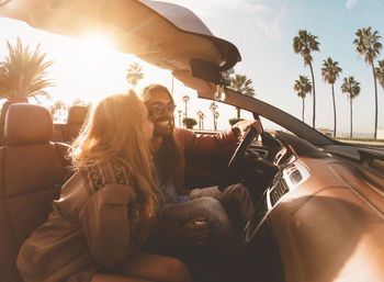 Young woman sitting in car against sky