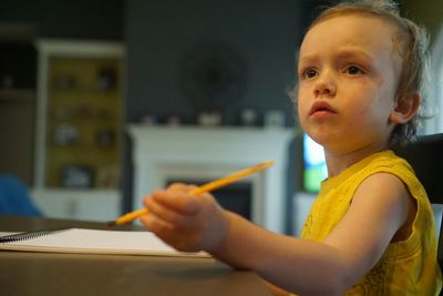 Boy holding pencil while sitting on table at home