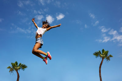 Low angle view of girl jumping against blue sky
