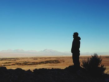 Man standing on landscape against clear blue sky