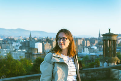 Young woman looking away while standing against cityscape