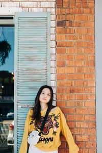 Portrait of woman standing against brick wall