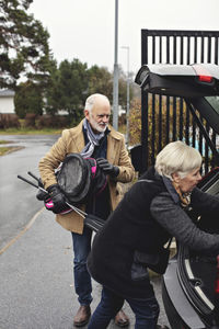 Senior man holding golf club while partner standing by car trunk during winter