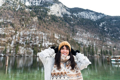 Young woman in winter sweater smiling, standing by a lake.