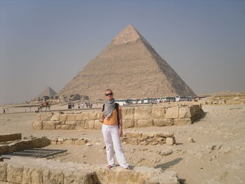 Young woman standing by giza pyramids against clear sky