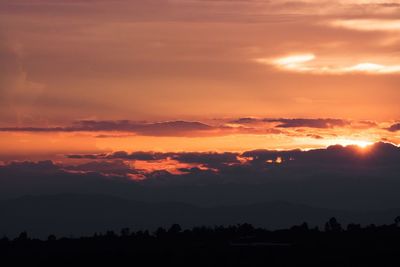 Scenic view of dramatic sky over silhouette landscape during sunset