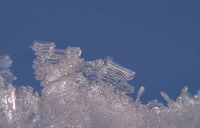 Close-up of frozen glass against blue sky