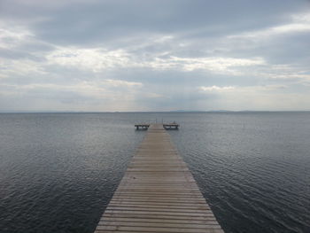 Pier on sea against cloudy sky