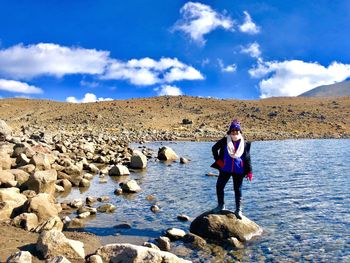 Full length of woman standing on rock at lake