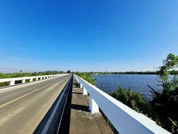 Road by river against clear blue sky