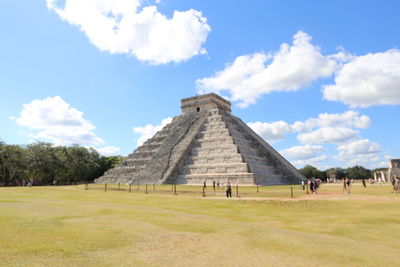 Tourists on field against cloudy sky