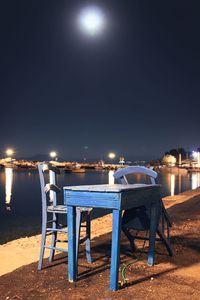 Empty chairs and tables at beach against sky at night