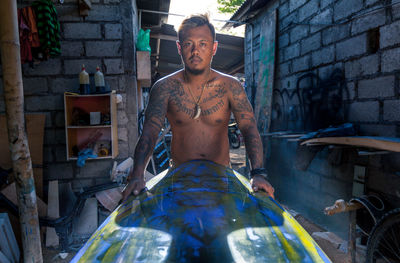 Portrait of serious tattooed man holding surfboard