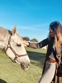 Smiling mature woman standing with horse on field against sky