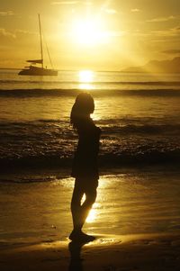 Silhouette boy standing on beach against sky during sunset