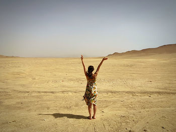Full length of woman with arms raised standing in desert