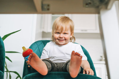 Cute funny little baby girl in chair for feeding at the bright kitchen at home