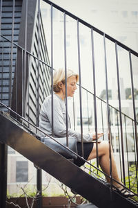 Side view of businesswoman using smart phone while sitting on steps at office yard