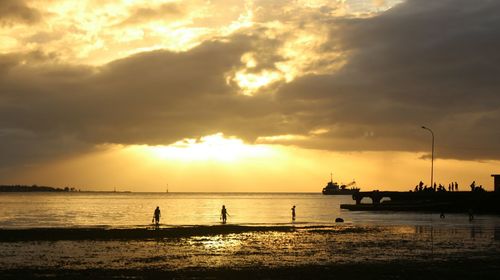 Silhouette people on beach against sky during sunset