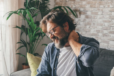 Man holding neck while sitting at home