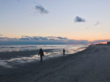 Silhouette people walking on beach against sky during sunset