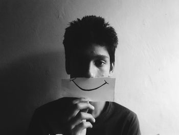 Portrait of boy holding paper with smiley against wall