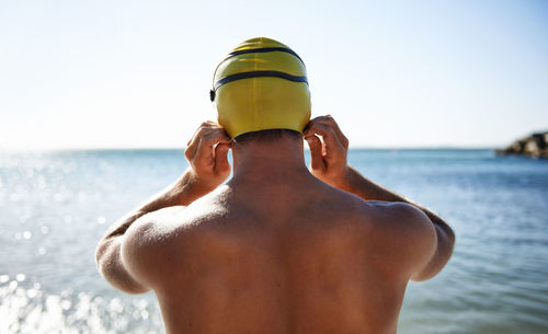Rear view of shirtless man holding water against sea