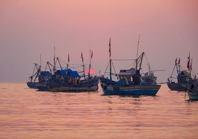 Boats moored in sea against clear sky at sunset