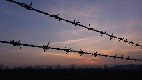 Barbed wire fence against sky during sunset