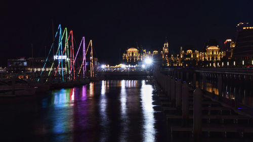 Illuminated bridge over river against buildings at night