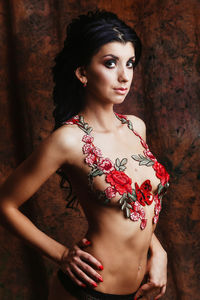 Portrait of shirtless young woman with floral decoration standing against wall