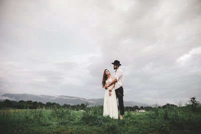 Young couple standing on field against sky