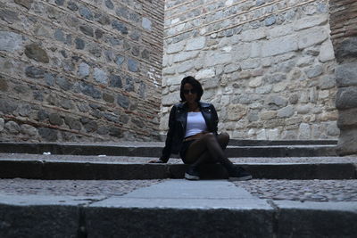 Full length portrait of woman sitting against wall