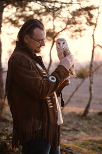 Man and wild bird over sunset sky in forest looking on each other owl symbol of power, wisdom wealth