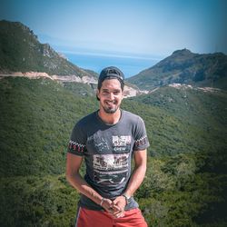 Portrait of young man standing on mountain against sky