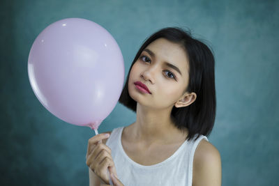 Portrait of young woman holding balloons against blue background