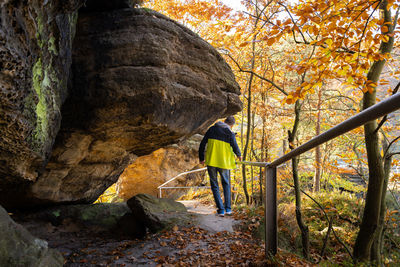 Rear view of adult man walking under sandstone rock formation in bohemian switzerland, czech rep