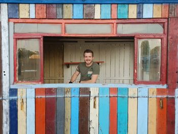 Portrait of man smiling seen through window amidst colorful wall