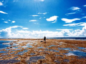 Man at beach against cloudy sky during sunny day