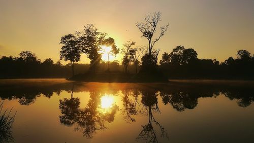 Silhouette trees by lake against sky during sunset